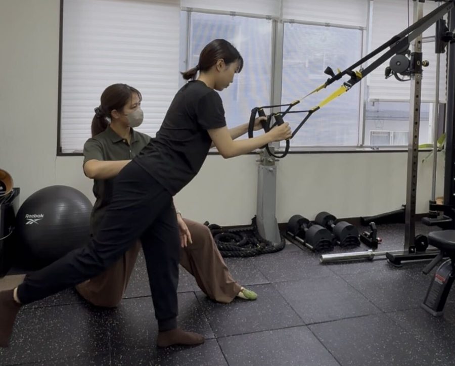 トレーナーの補助でサスペンショントレーニングをする女性