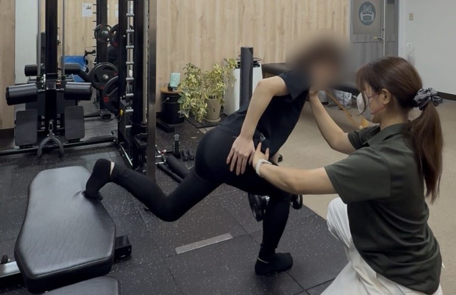 トレーナーがフォームを支えながらトレーニングする様子
